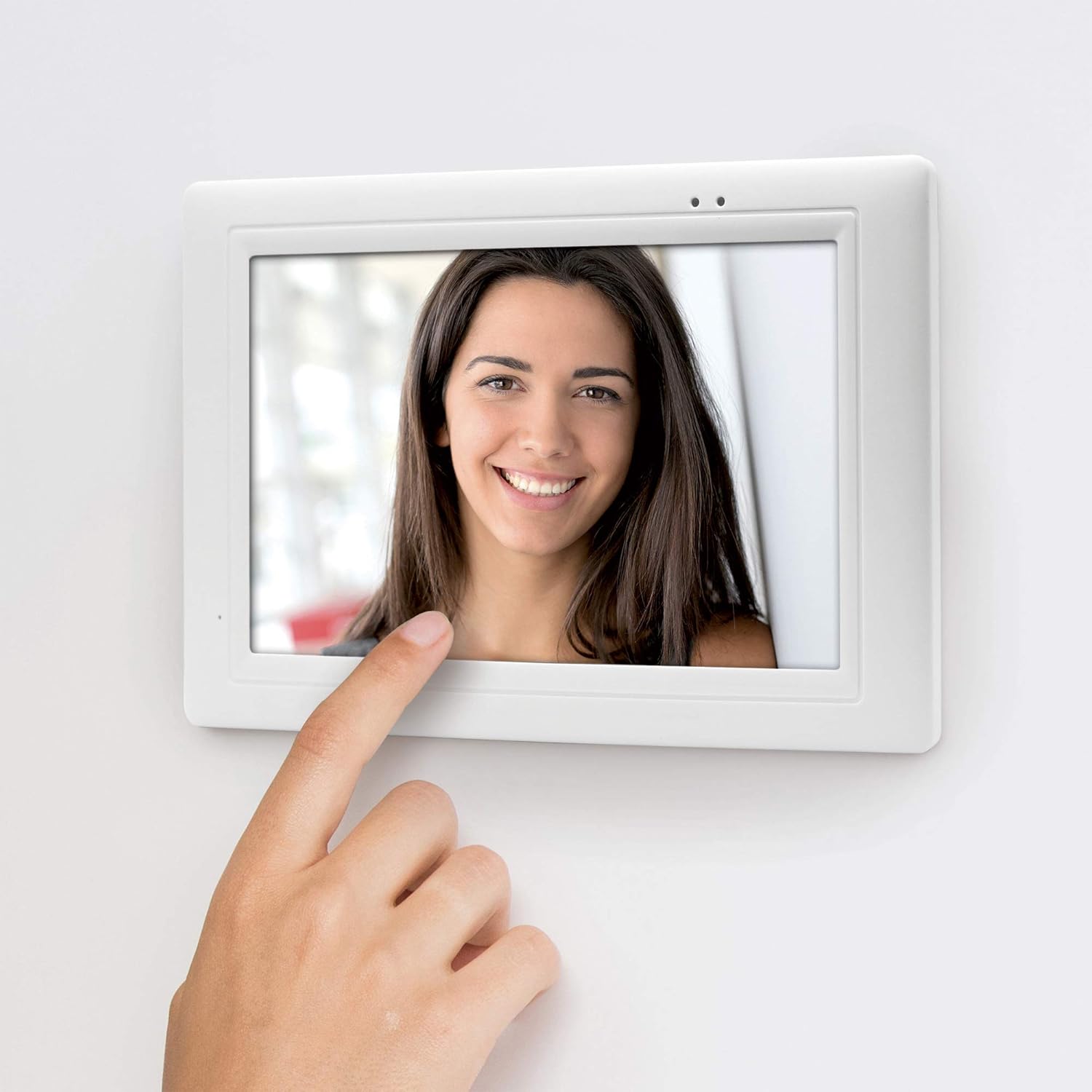 A hand interacting with the touchscreen of the Thomson Wireless Video Doorphone indoor monitor, showing a visitor's face.
