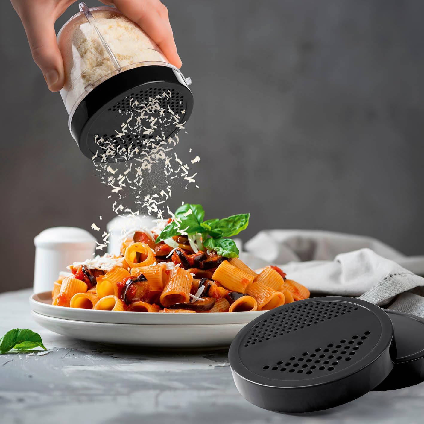 A hand using the GOURMETmaxx Mr. Magic Power Pro Blender cup with a sprinkling lid to add grated cheese to pasta.
