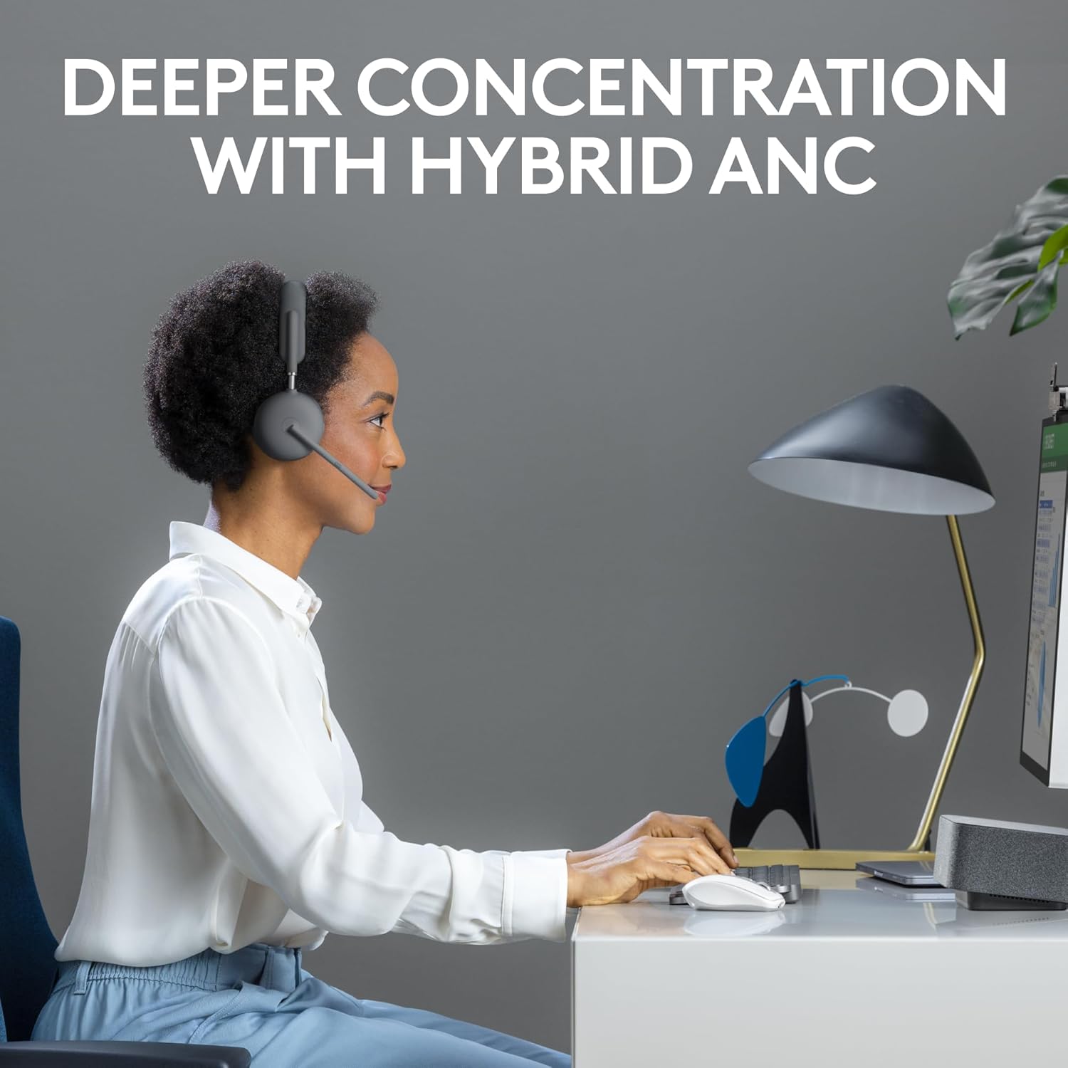 A woman wearing the Logitech Zone Wireless 2 headset, focused on her computer screen in an office setting, illustrating deeper concentration with hybrid ANC.
