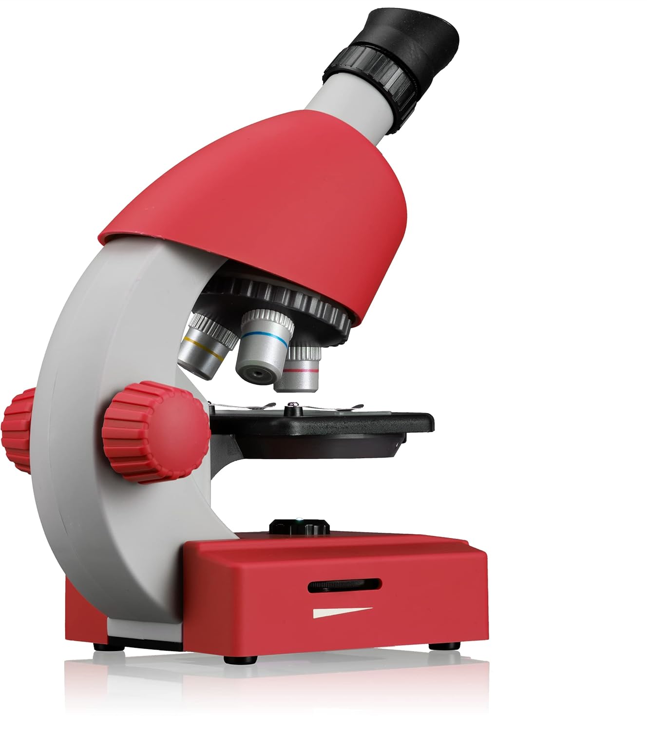 Samping view of the red Bresser Junior Microscope, showing the objective lenses and focus knobs.