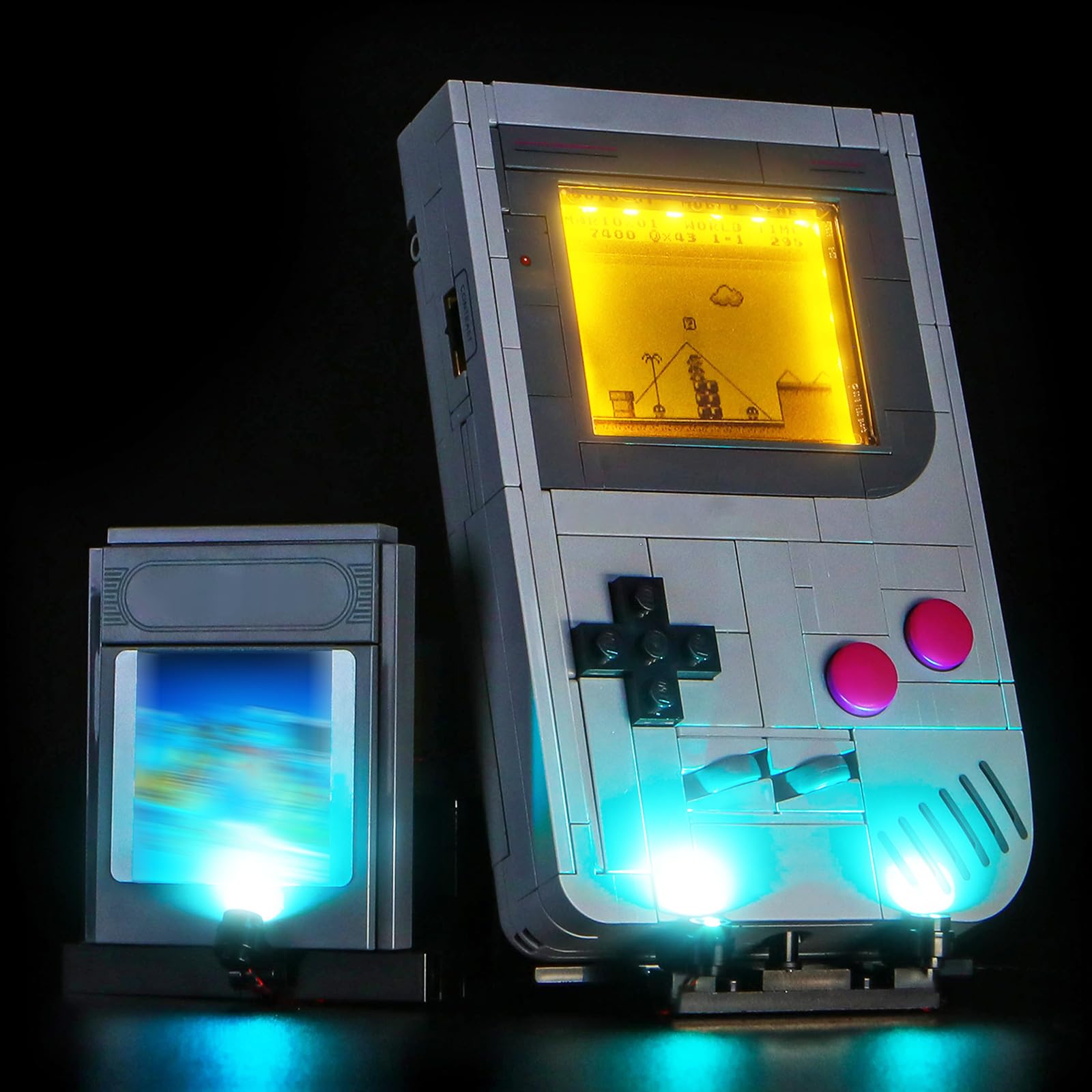 A LEGO Game Boy model with an illuminated screen and glowing lights at the bottom, standing next to a smaller illuminated LEGO game cartridge.