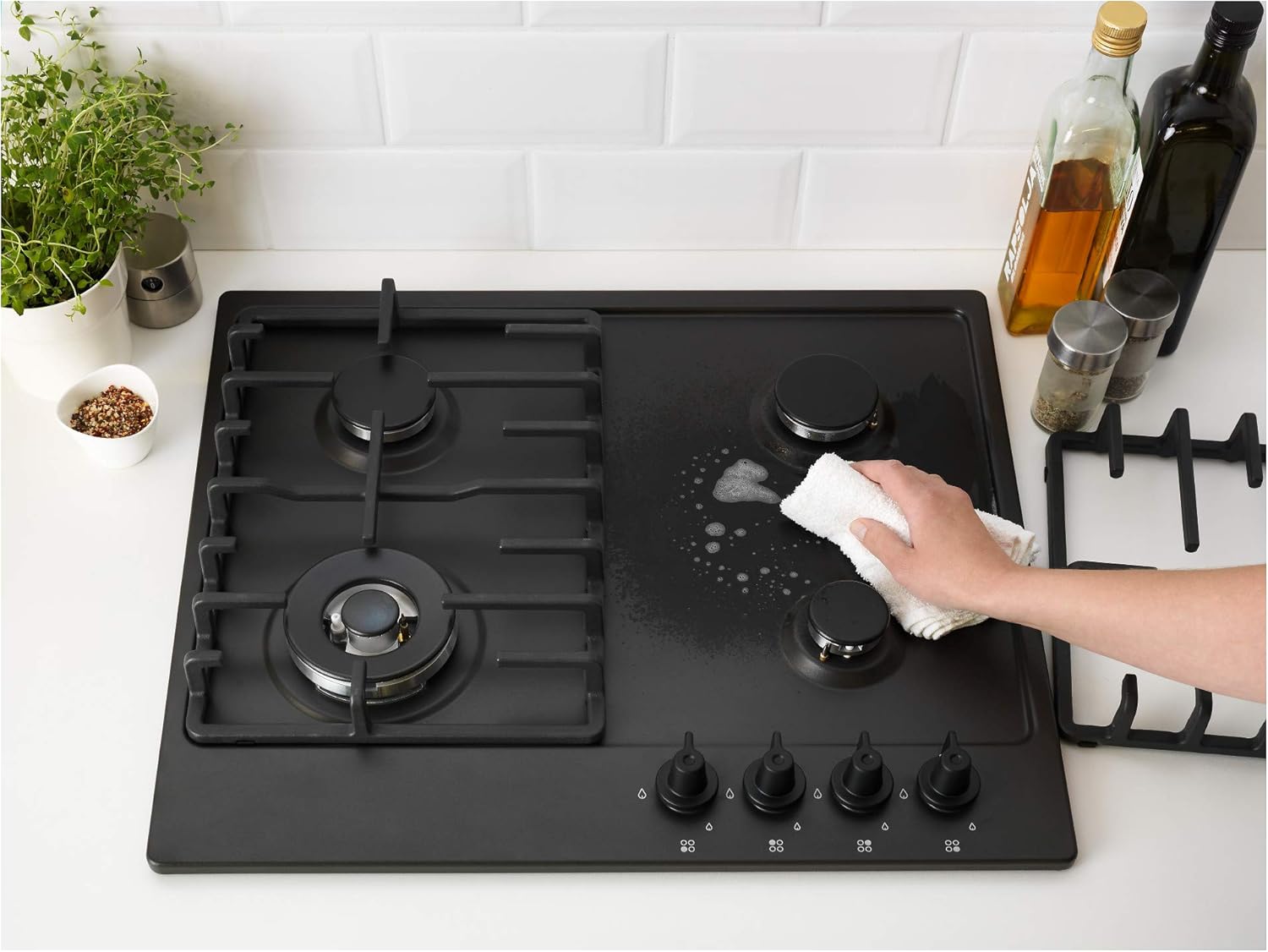 A hand cleaning the surface of the LivSLåga gas hob with a white cloth and soapy water.