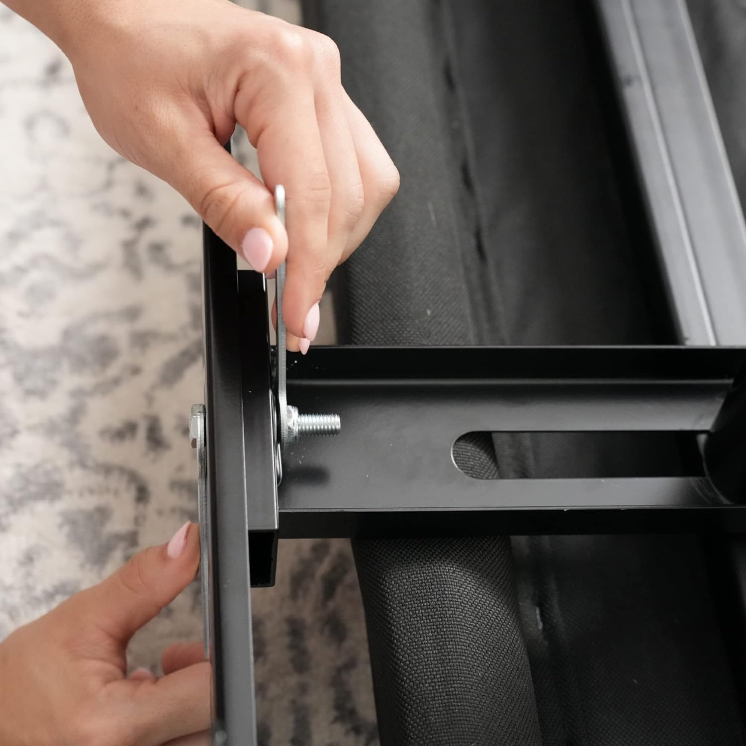 A close-up of a person's hands securing a headboard to the installed bracket on the bed frame using a bolt and washer.