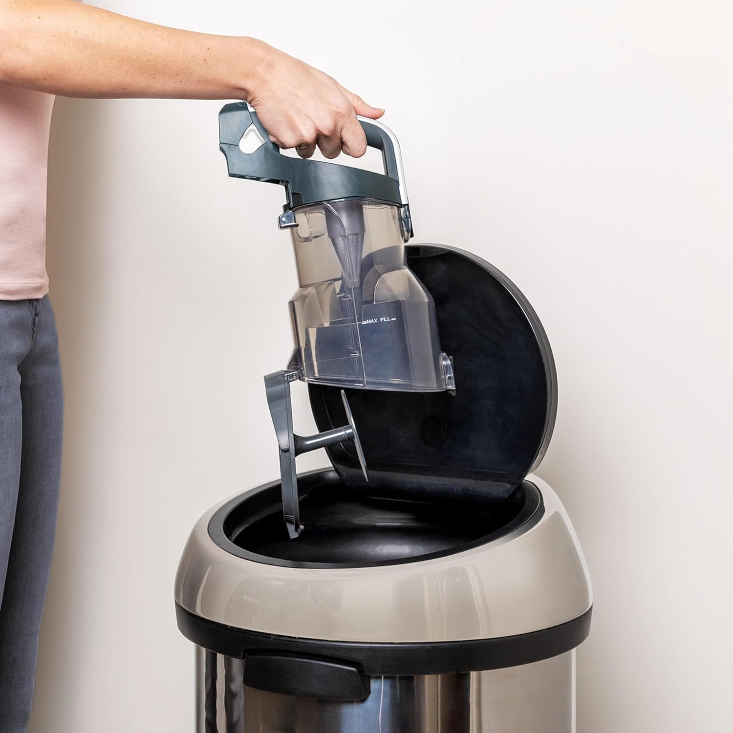 Hand emptying the dust cup of the Shark vacuum into a trash bin