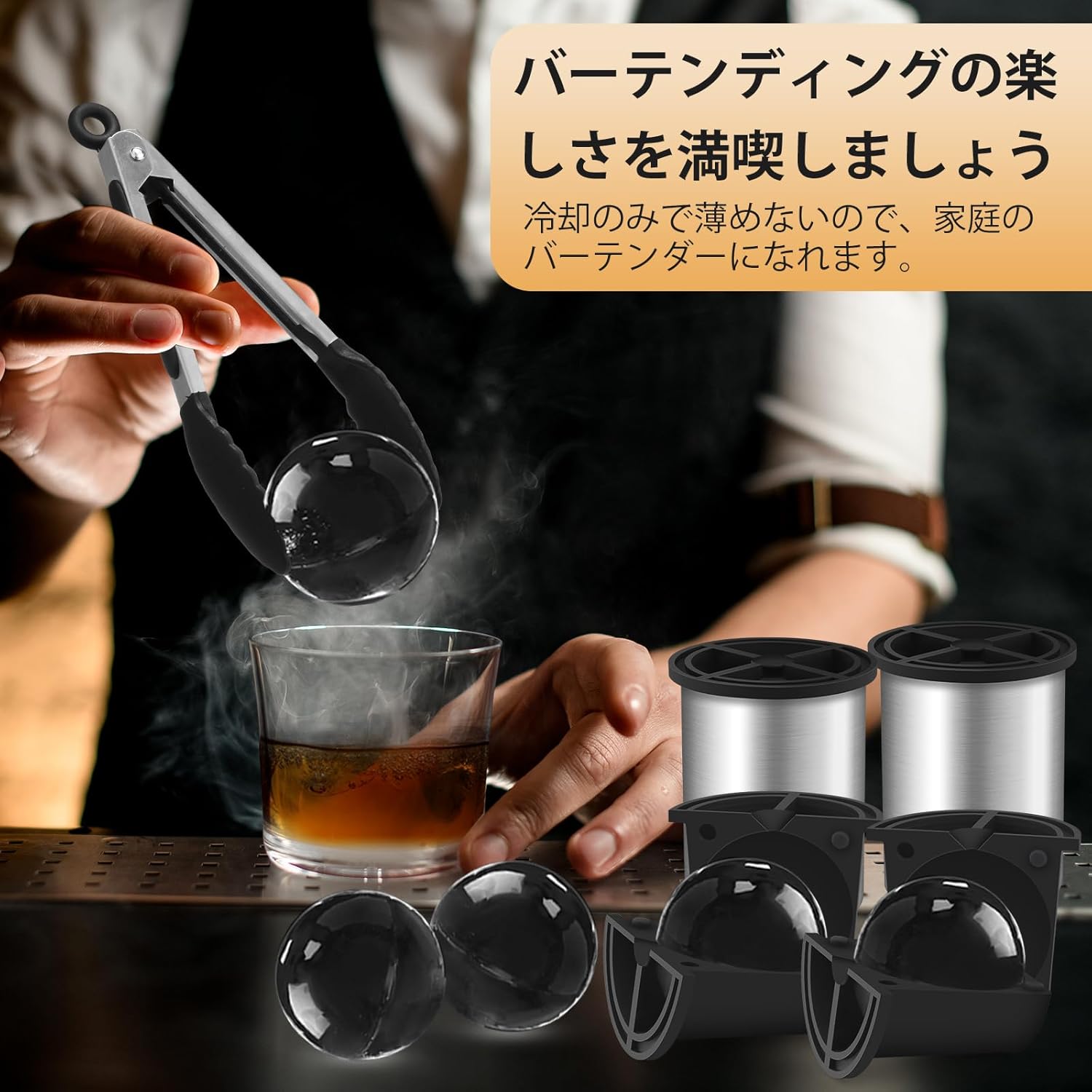 A hand using ice tongs to place a clear ice ball into a glass of amber liquid.