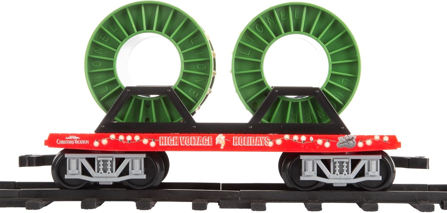 The flatcar carrying two large green reels, representing Christmas lights, on the train track.