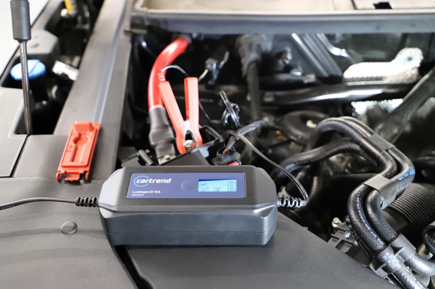 Cartrend battery charger connected to a car battery in an engine bay, showing the display