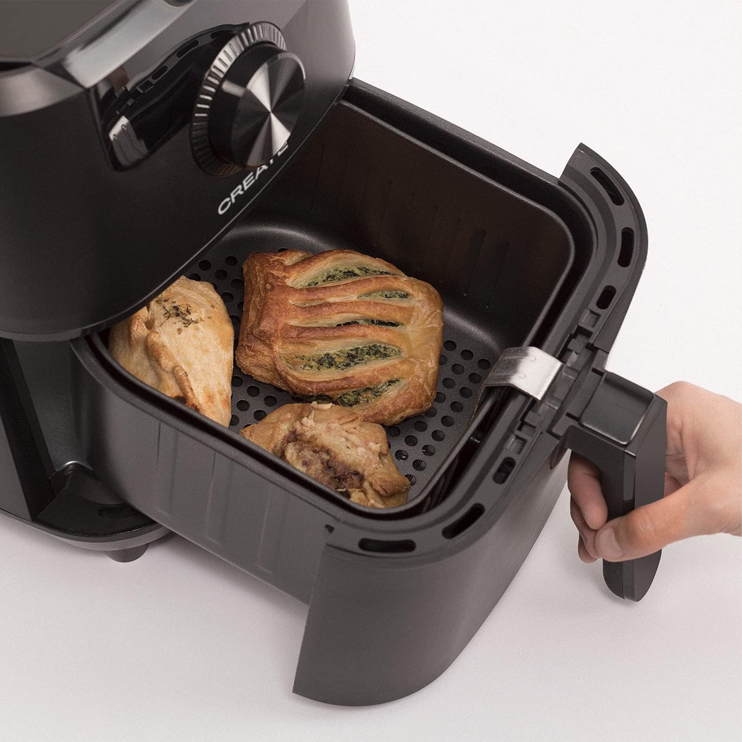 Air fryer basket pulled out, showing cooked pastries and chicken inside.