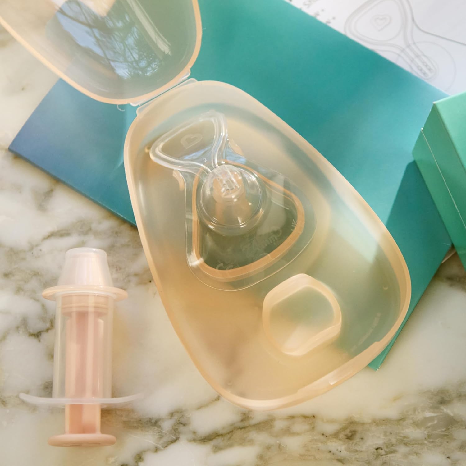 Munchkin Flow Nipple Shield +, travel case, and cleaning syringe laid out on a surface, ready for cleaning or storage.