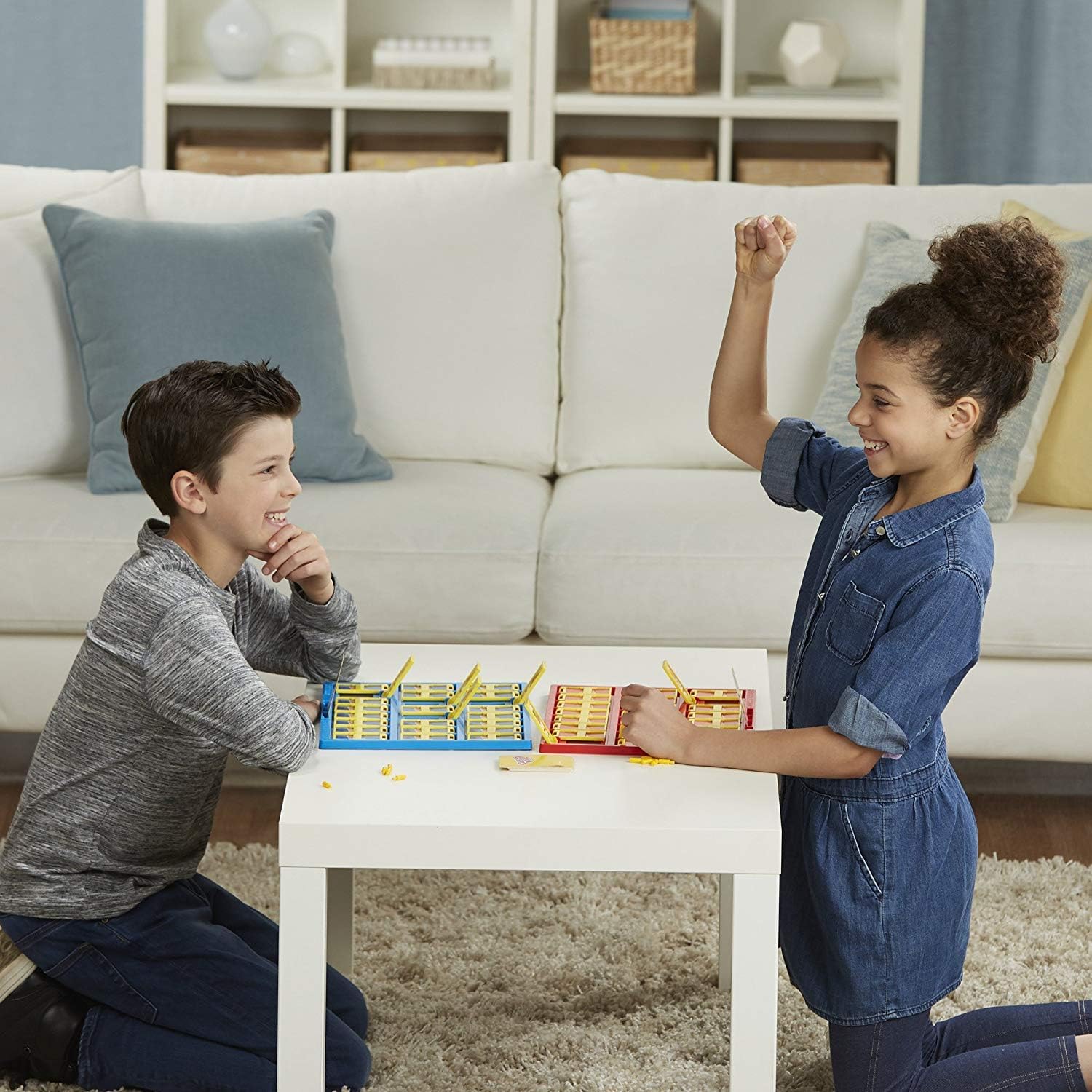 Two children playing the Guess Who game, seated at a table.