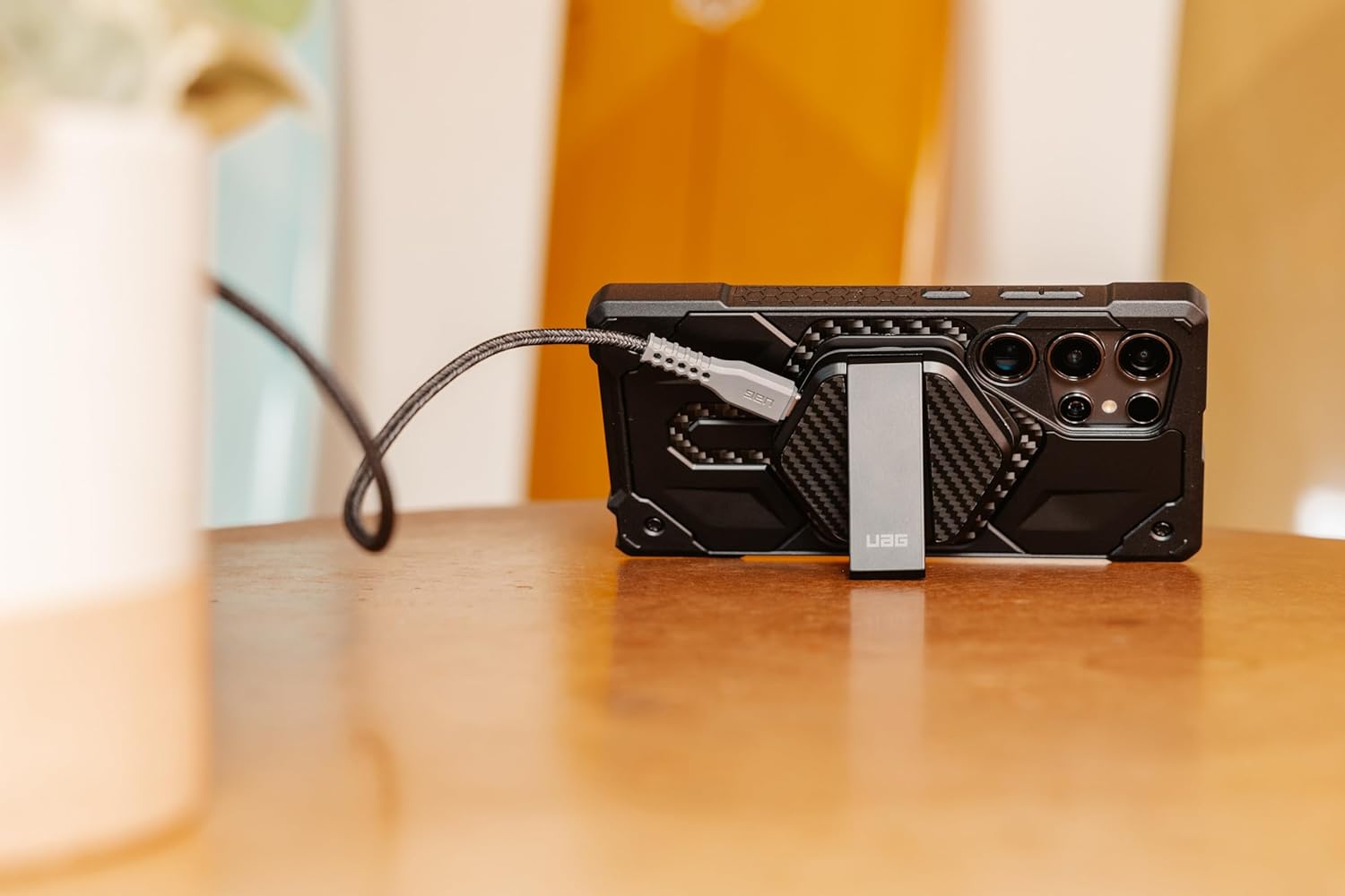 Side view of UAG Wireless Charging Pad with kickstand supporting a smartphone