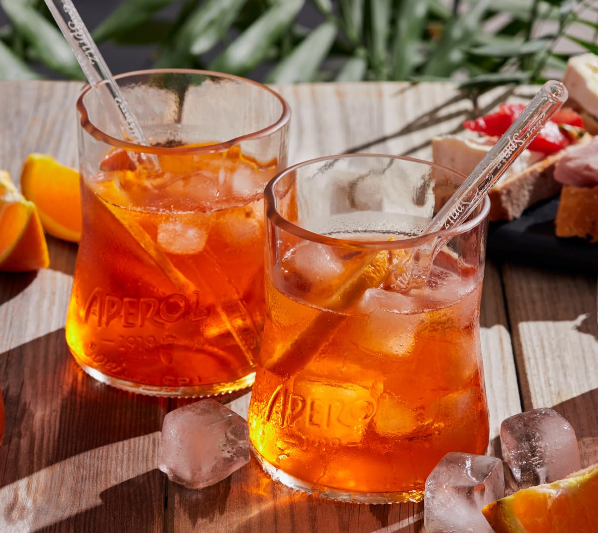 Aperol Spritz Set aus recycelten Flaschen: zwei Glaser mit kunstvoll geformten Randern und zwei Glasstronhhalme