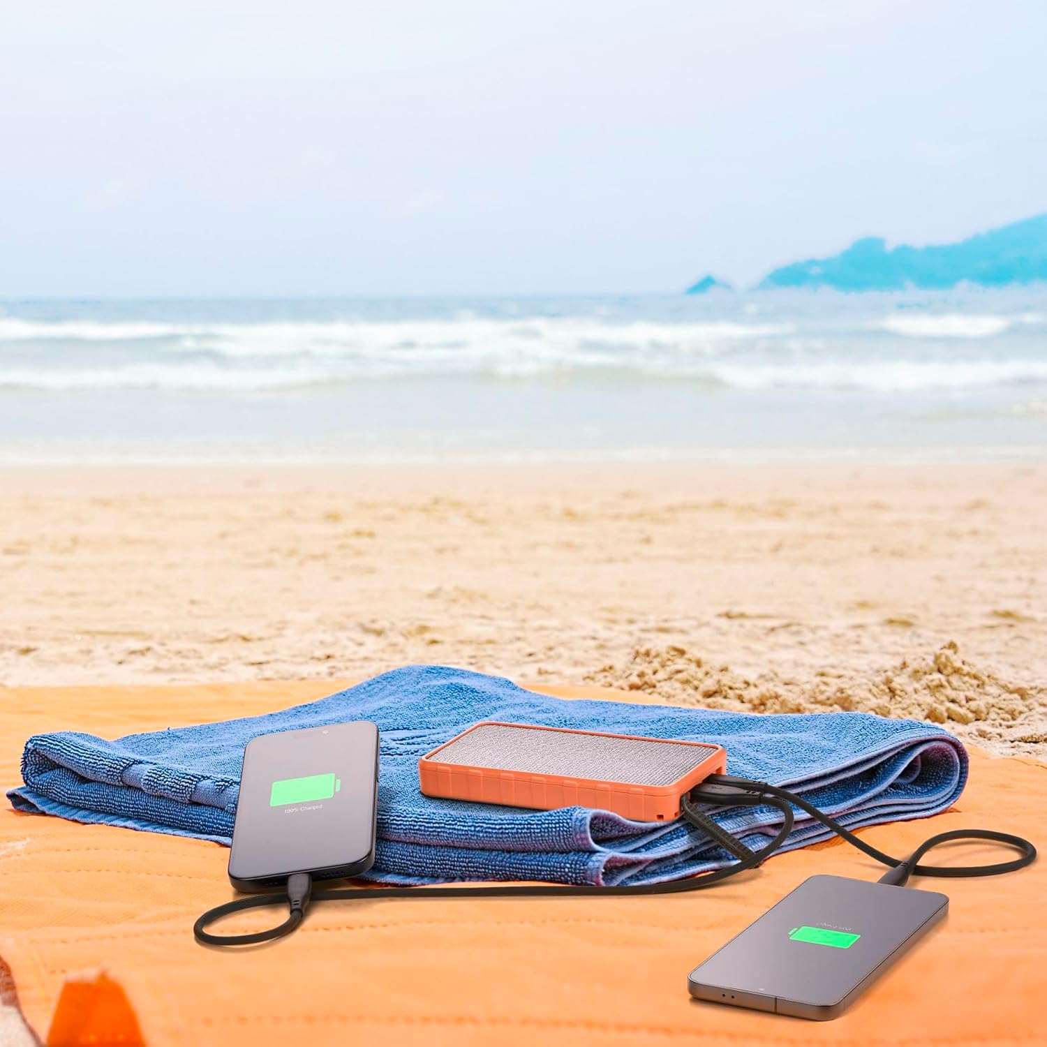 Power Bank Cellularline ładuje dwa urządzenia energią słoneczną na ręczniku plażowym.