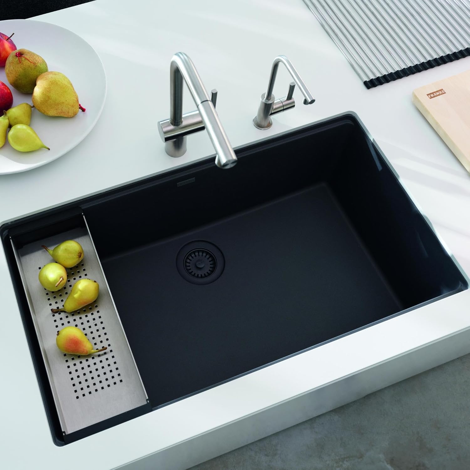 Modern kitchen sink with a black Franke Colorline basket strainer, surrounded by kitchen accessories and fresh fruit.