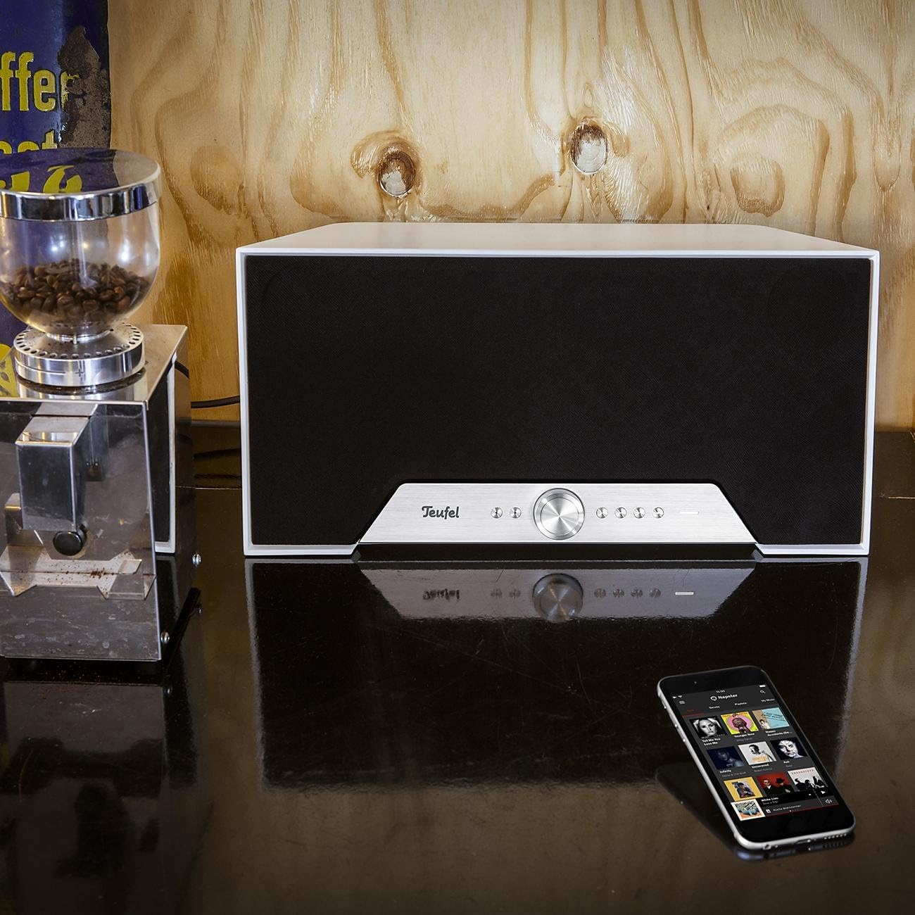 Teufel One M speaker in a living room setting, demonstrating its aesthetic integration and use with a smartphone for control.