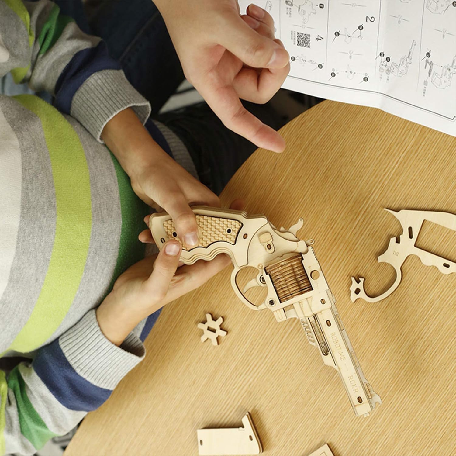 Hands assembling the wooden puzzle gun with instructions