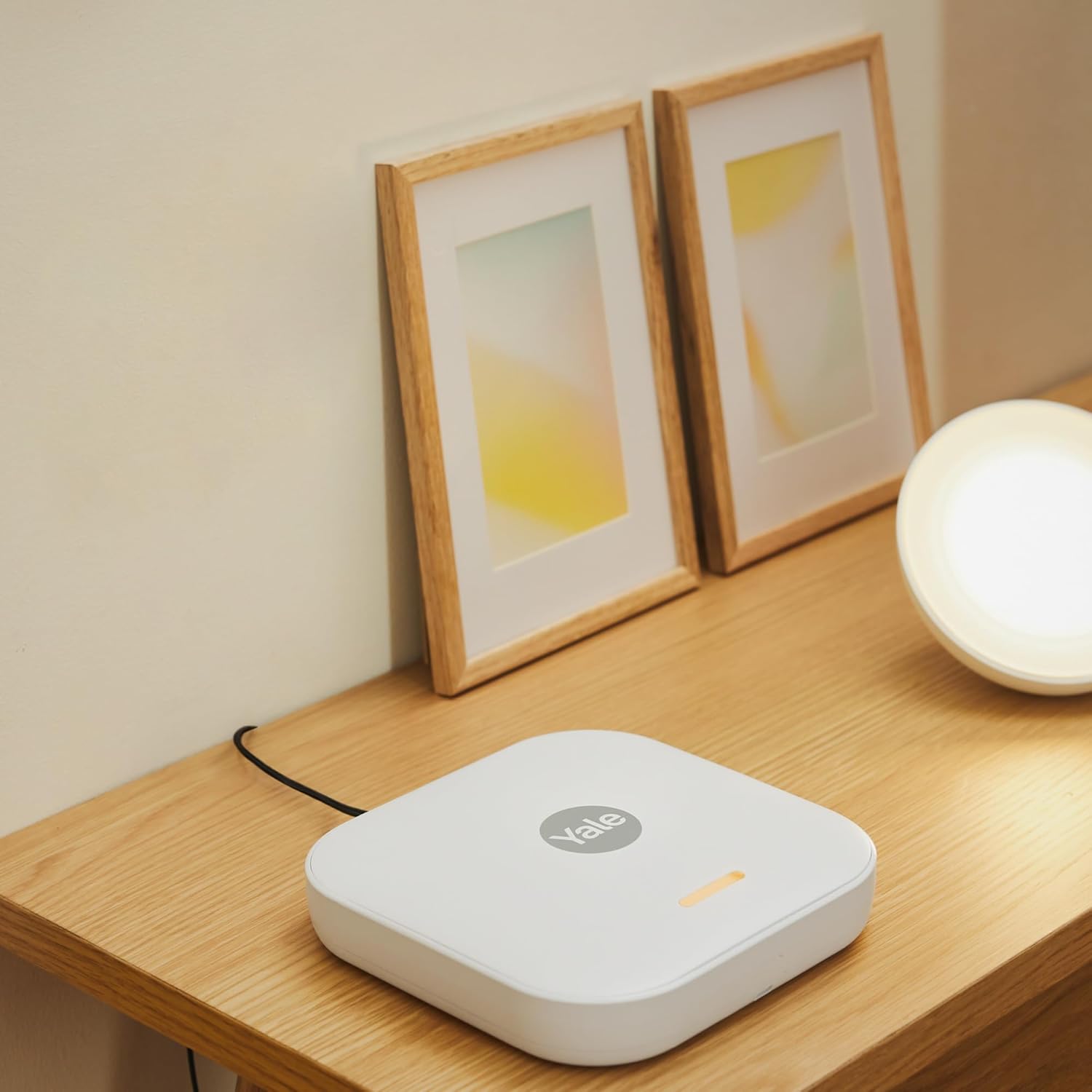Yale Smart Alarm Hub placed on a wooden table next to framed pictures.