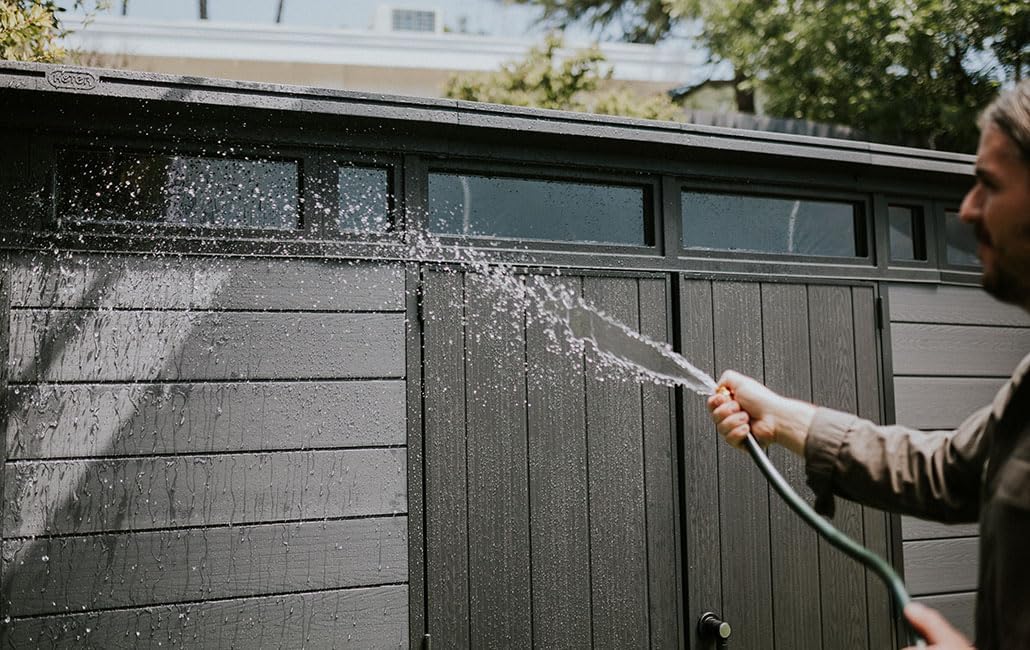 A person spraying water to clean the exterior of the Keter Cortina 117 Garden Shed