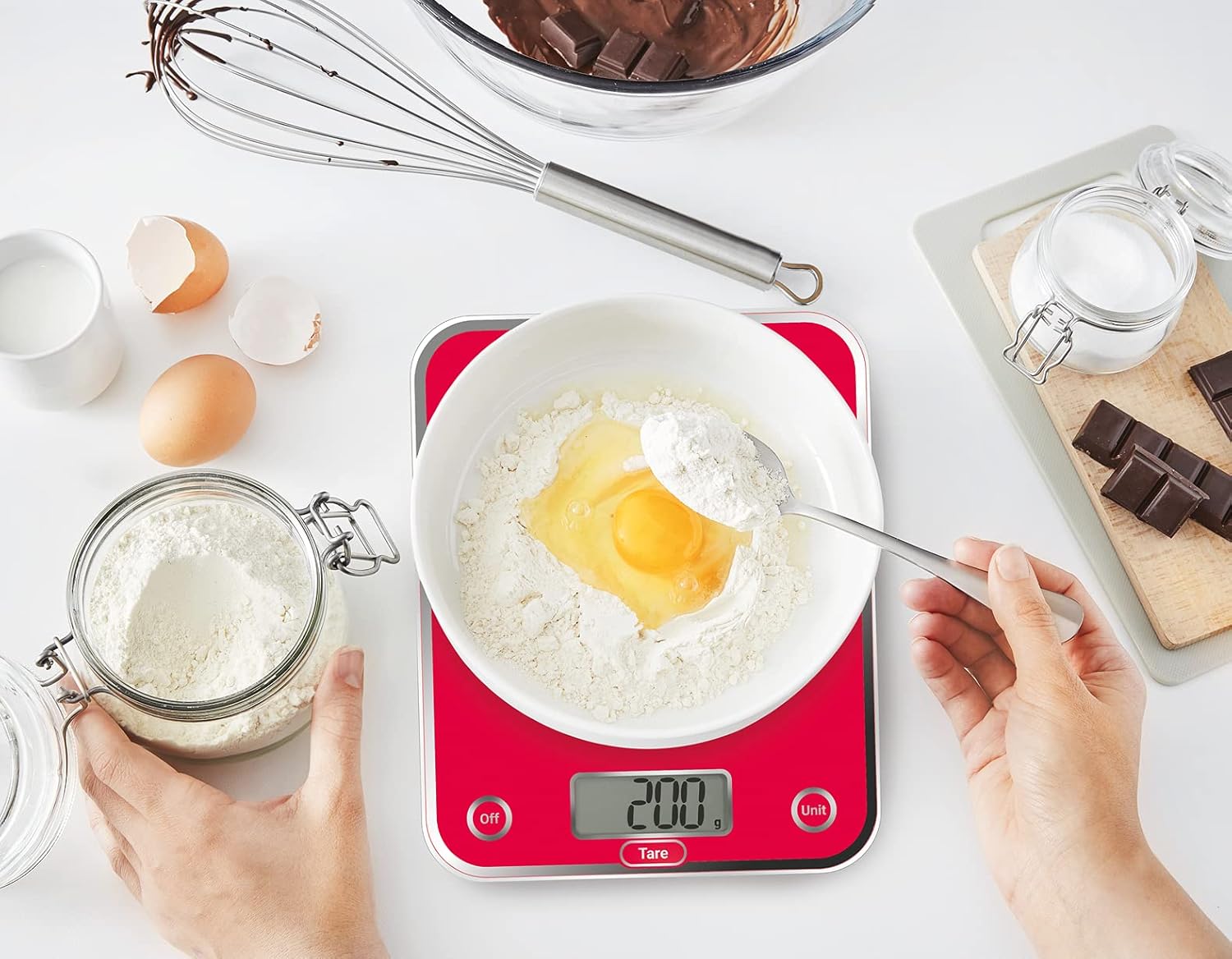 Hands placing flour and an egg into a bowl on the Moulinex Optiss BN5003 kitchen scale, which displays 200g.