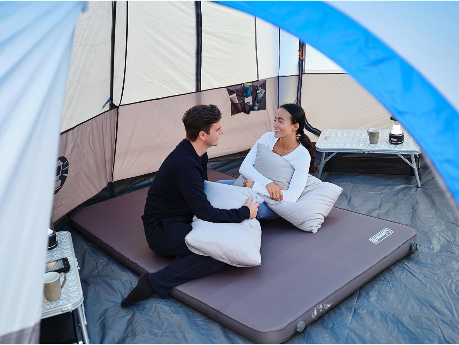 A couple relaxing on the mattress in a tent, enjoying beverages