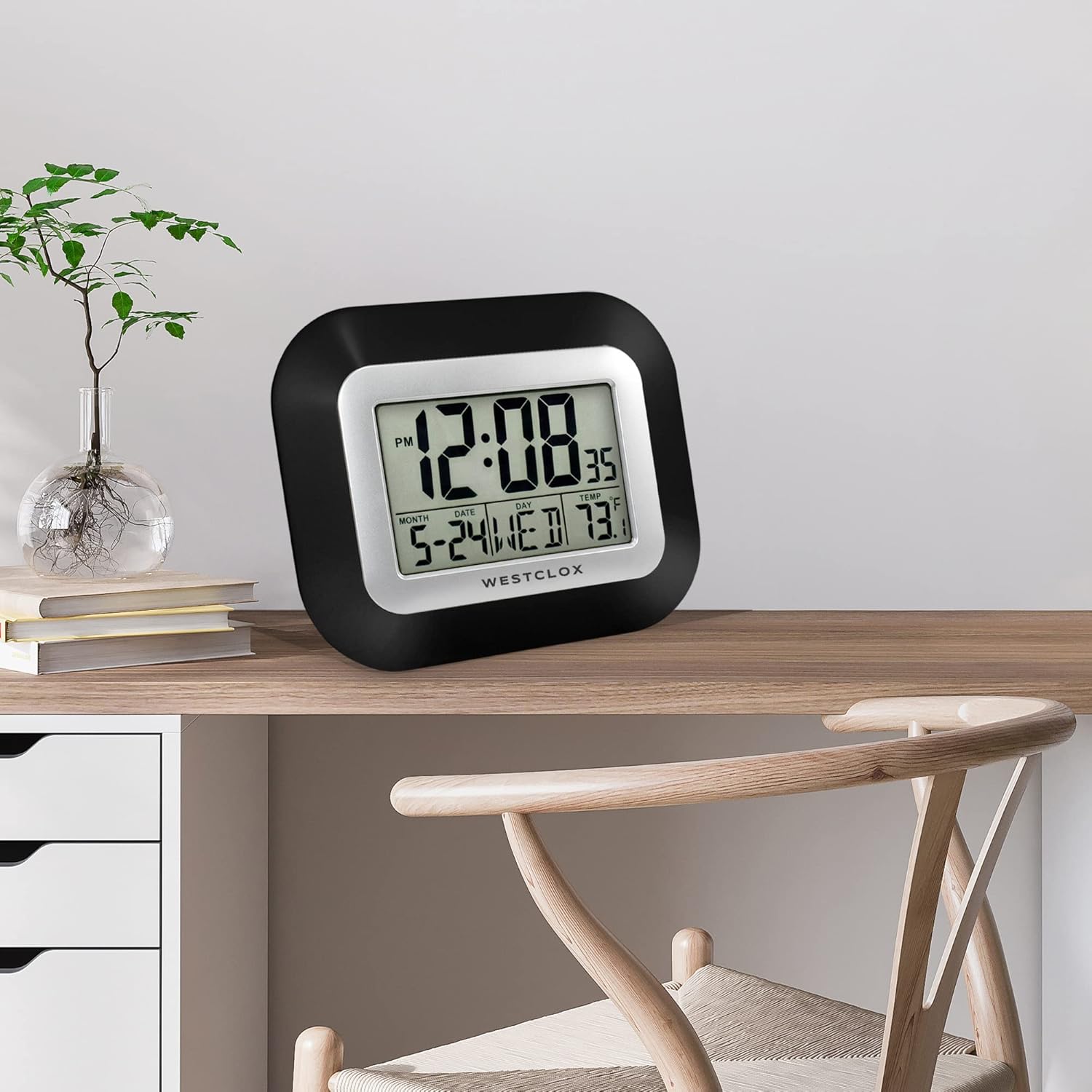 Westclox Digital Wall Clock placed on a wooden desk next to a plant and books.