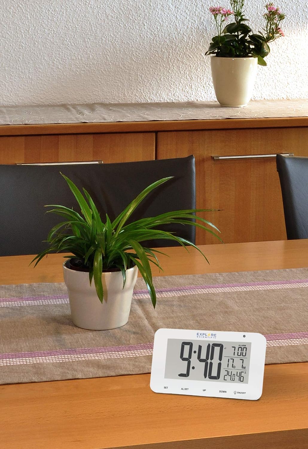 Explore Scientific RDC1004 Desk Clock placed on a wooden table in a home setting, next to a potted plant.