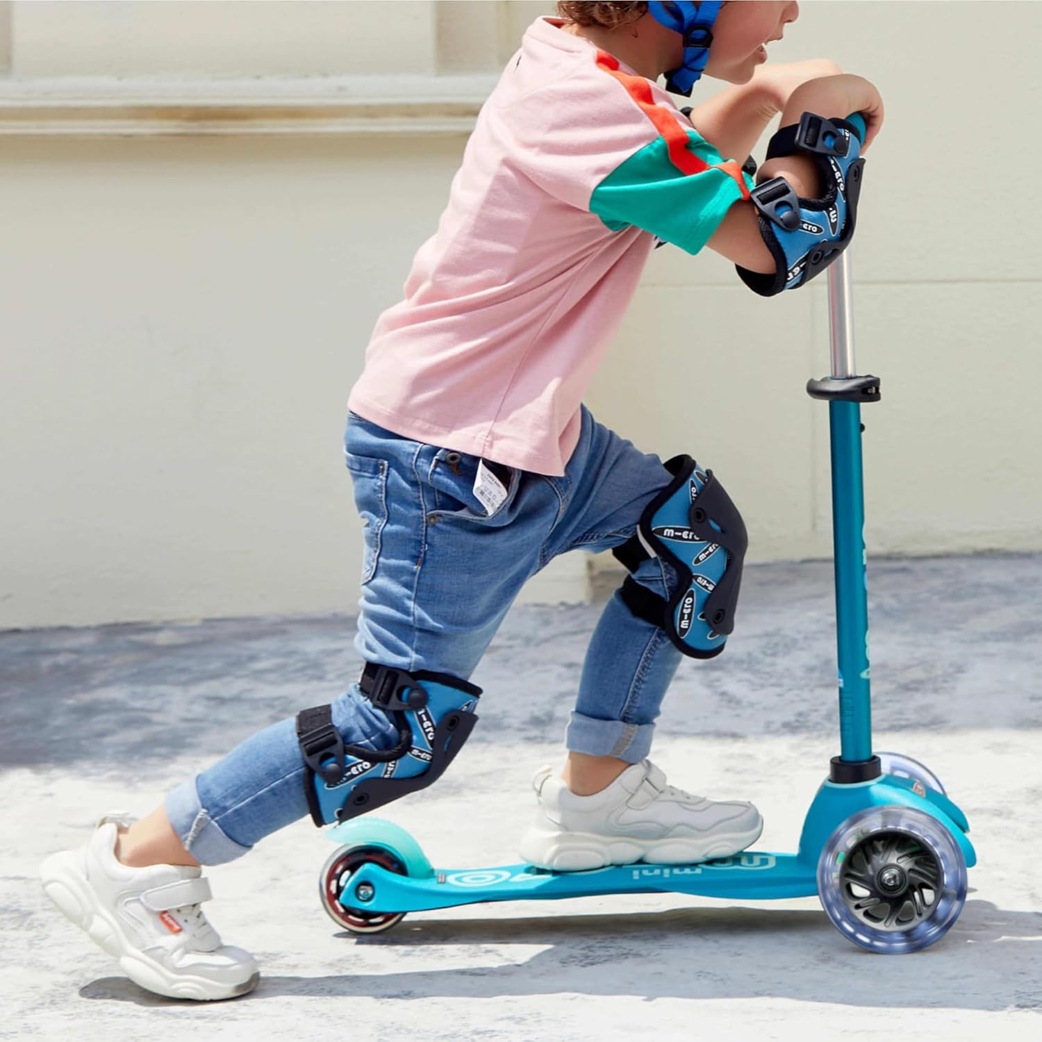 Child riding Micro Mini Deluxe scooter with helmet and pads