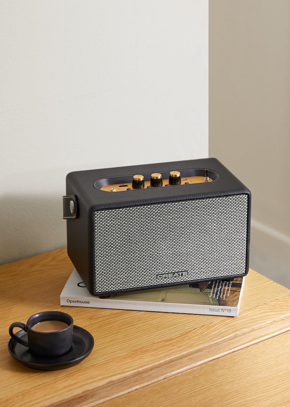 A person's hands holding a smartphone displaying a music player interface, with the CREATE Speaker Retro in the background, demonstrating Bluetooth connectivity.