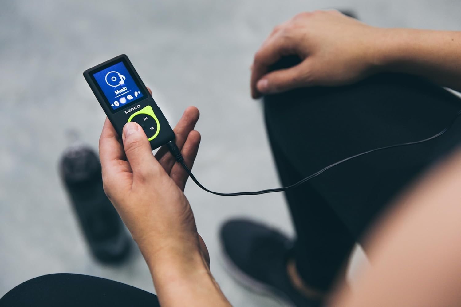 Person holding and using the Lenco Xemio-768 MP3/MP4 Player with wired headphones.
