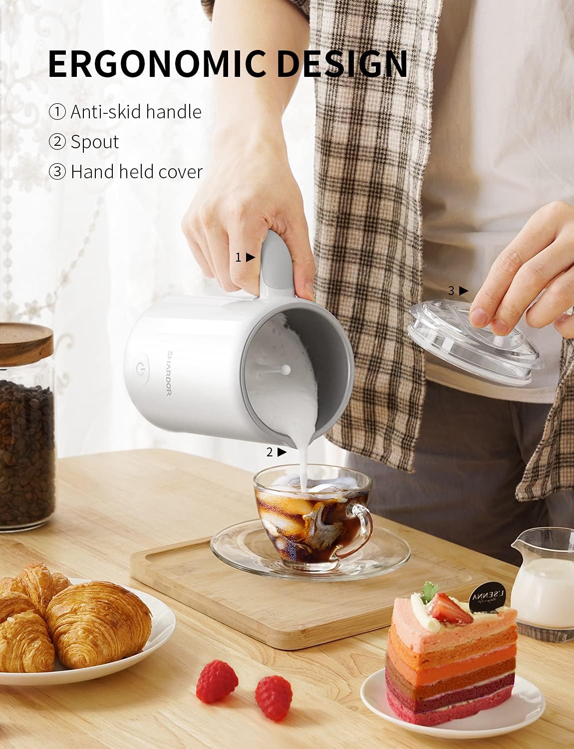 A person holding the SHARDOR milk frothing pitcher by its ergonomic handle, pouring frothed milk into a cup. The image highlights the anti-skid handle, spout, and handheld cover.