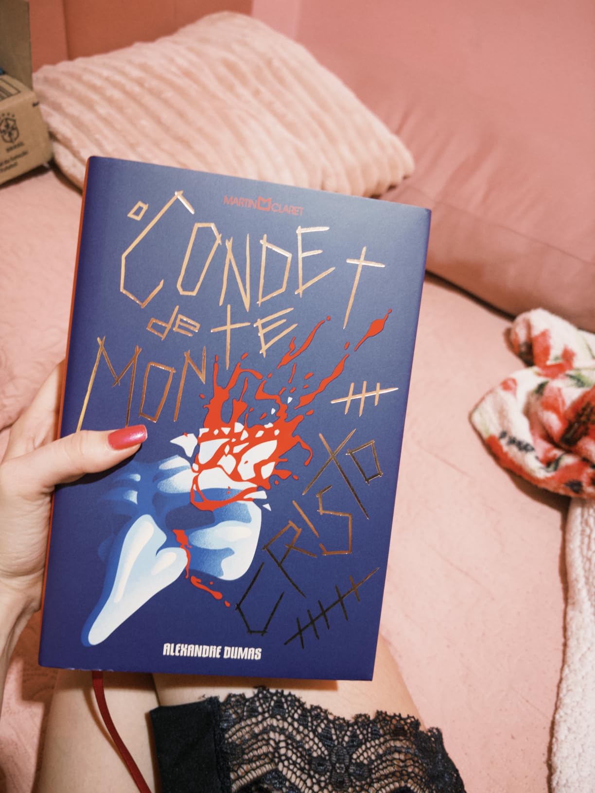 Mão segurando o livro O Conde de Monte-Cristo de capa azul com ilustração de punhal e sangue