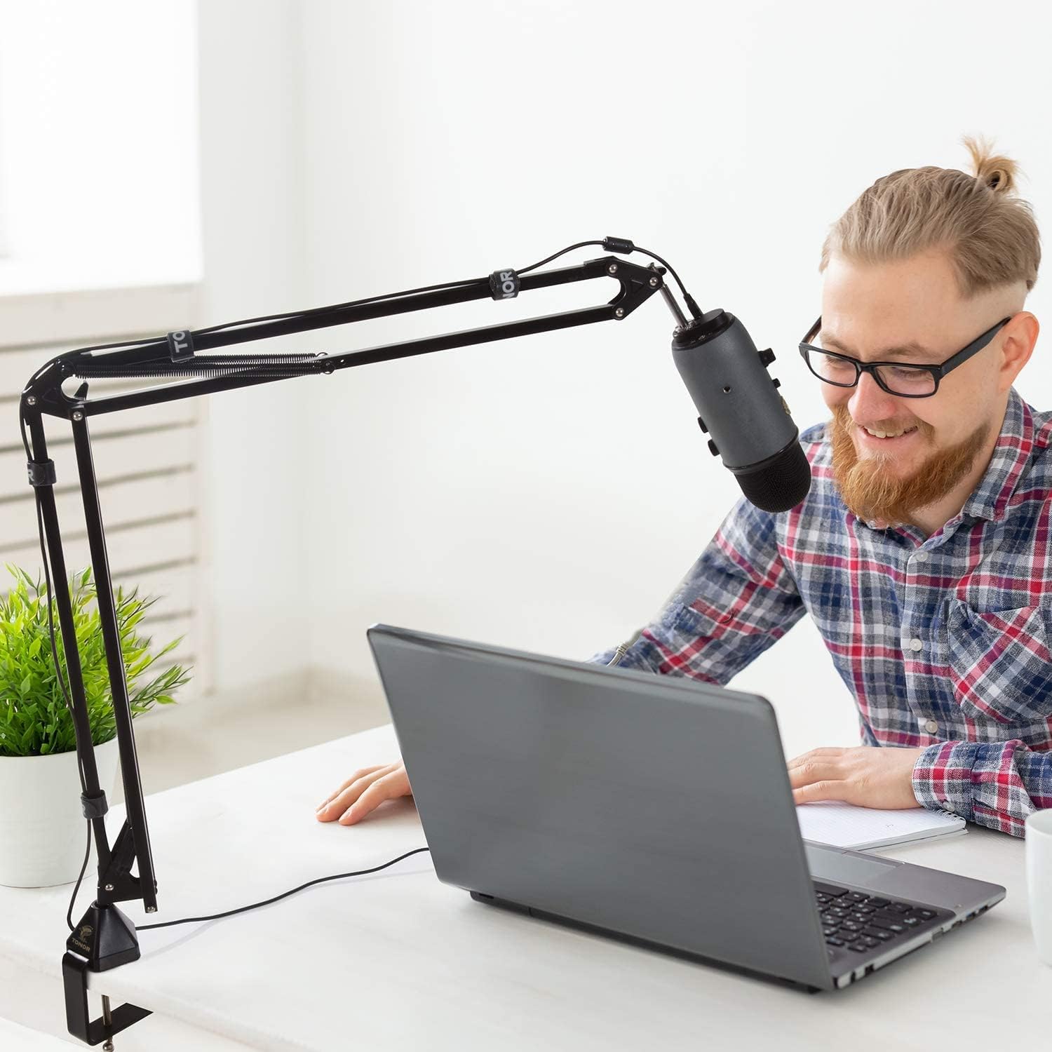 A person using the TONOR T30 microphone arm stand with a microphone attached, positioned over a desk with a laptop, illustrating typical usage.
