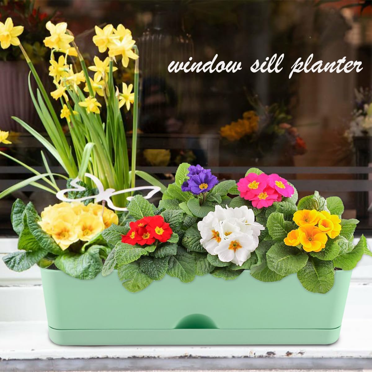 A green rectangular planter filled with various colorful flowers, placed on a window sill.
