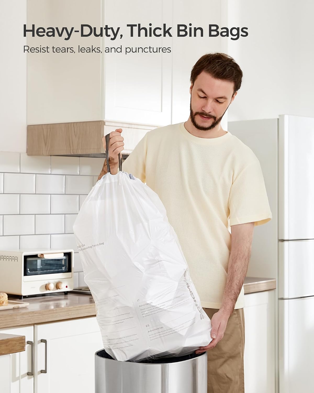 A man placing a white trash bag into a stainless steel trash can.