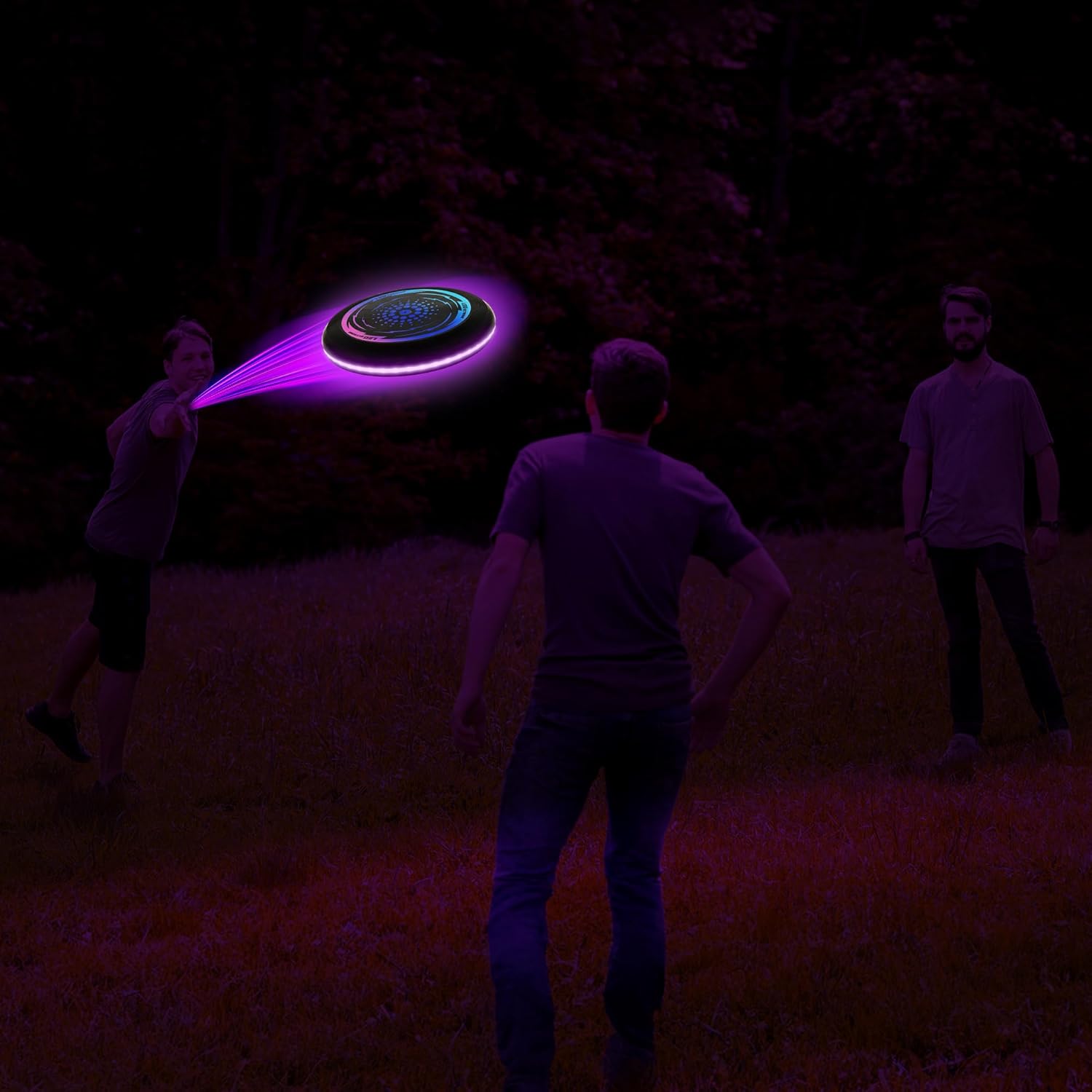Three people playing with the ArtCreativity Light Up Flying Disc Toy at night, with the disc glowing brightly