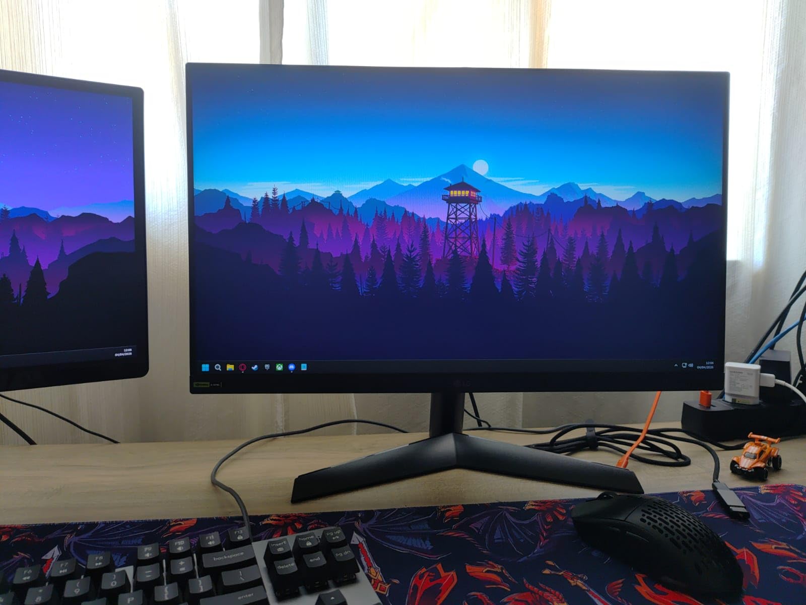Monitor LG UltraGear preto com tela exibindo um papel de parede com paisagem estilizada, posicionado em um setup de computador.