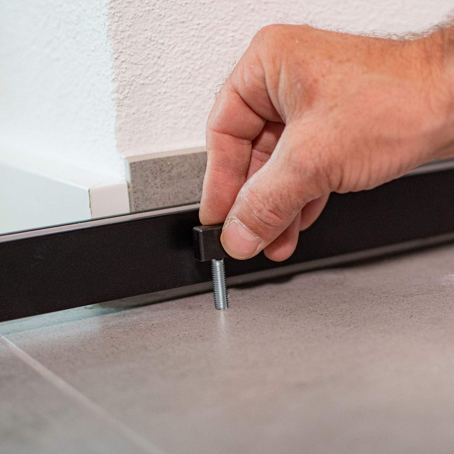 A hand adjusting the floor guide pin for the sliding door, showing the small black guide being screwed into the floor near the door's bottom edge.