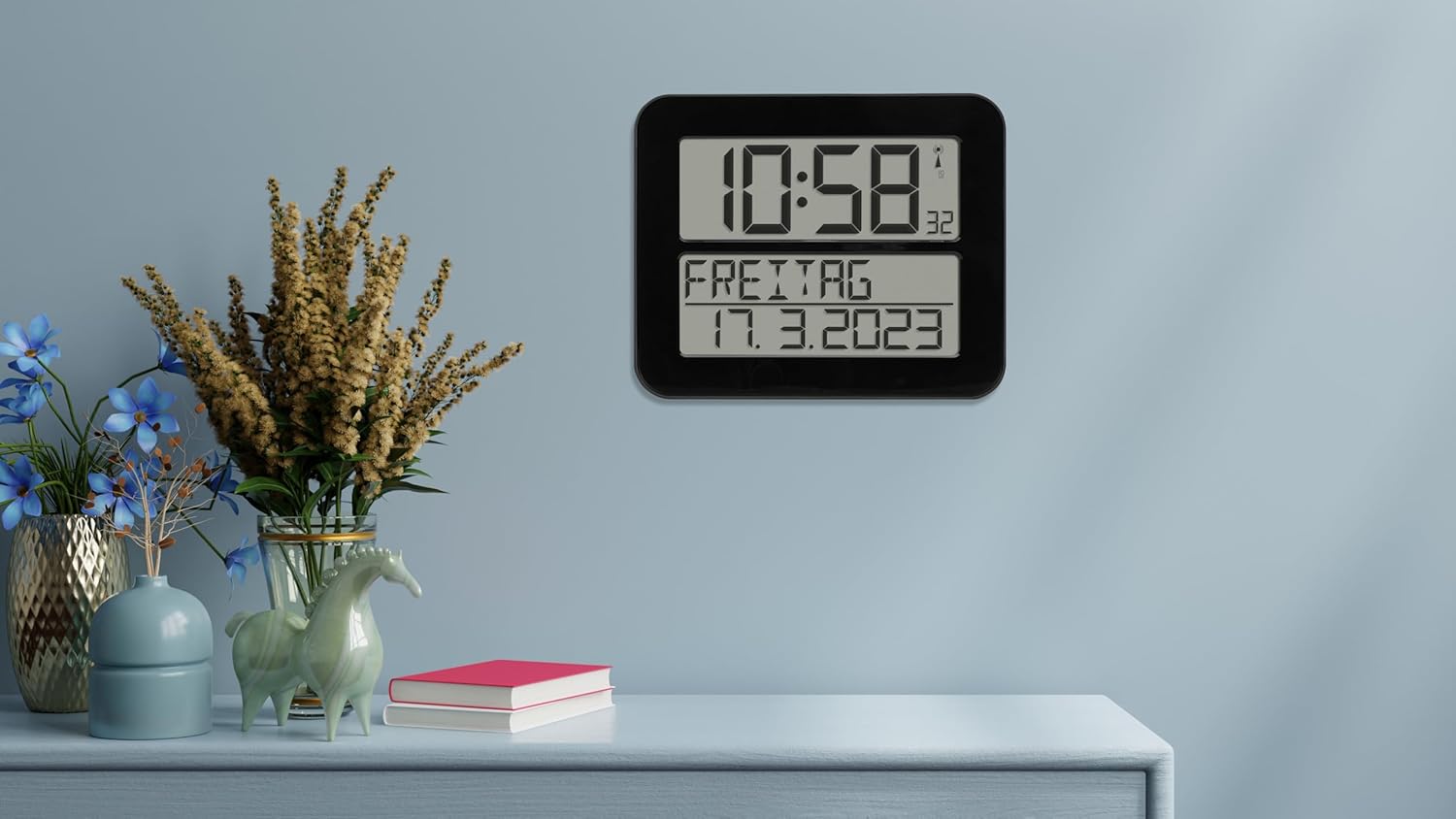 TFA Dostmann Timeline Max clock placed on a light blue desk next to decorative vases and books, demonstrating its use in a home or office setting.