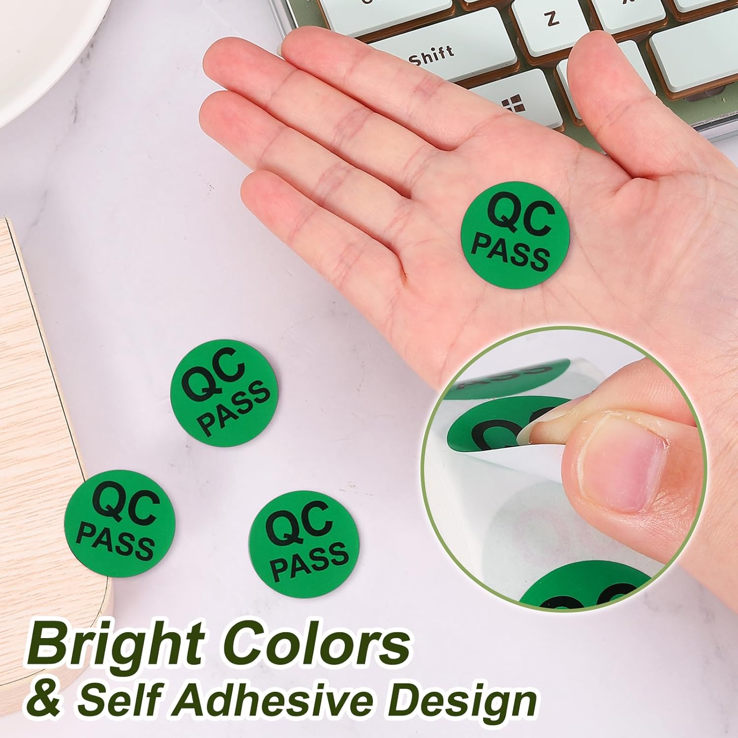 Hand holding a green QC Pass label, with other labels on a desk