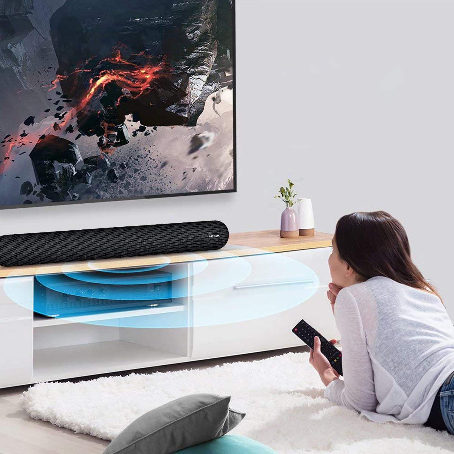 A person using the remote control to operate the Roxel RSB380 Soundbar, which is placed below a television.