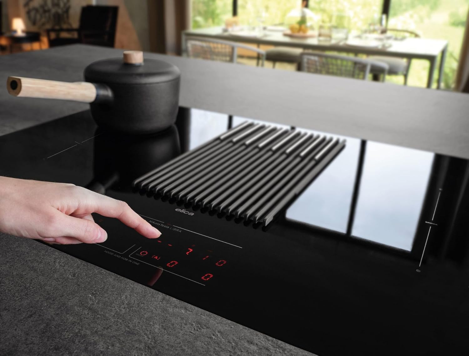 A hand adjusting the power settings on the Elica NikolaTesla Libra induction hob, with a pot on one of the cooking zones.