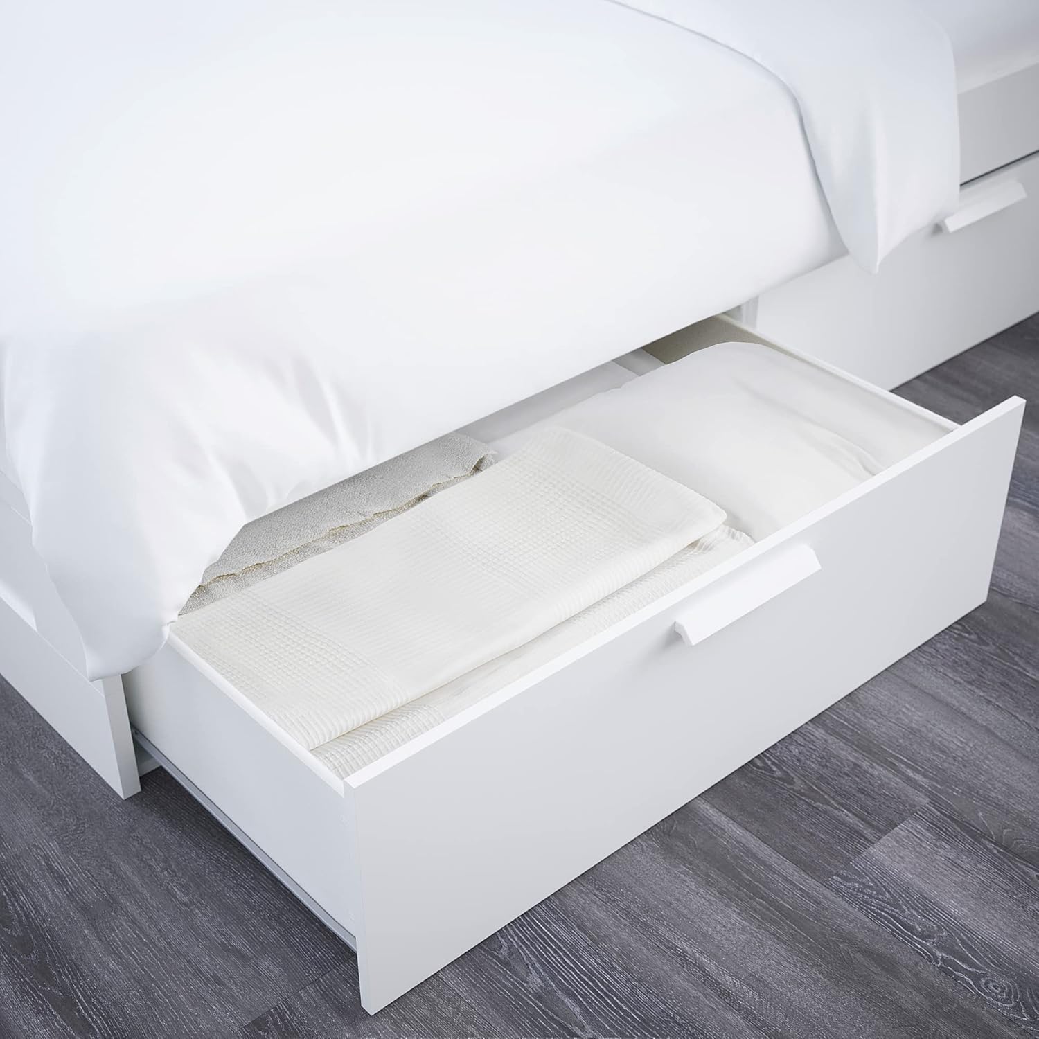 An open under-bed storage drawer of the BRIMNES bed frame, showing blankets and pillows stored inside.