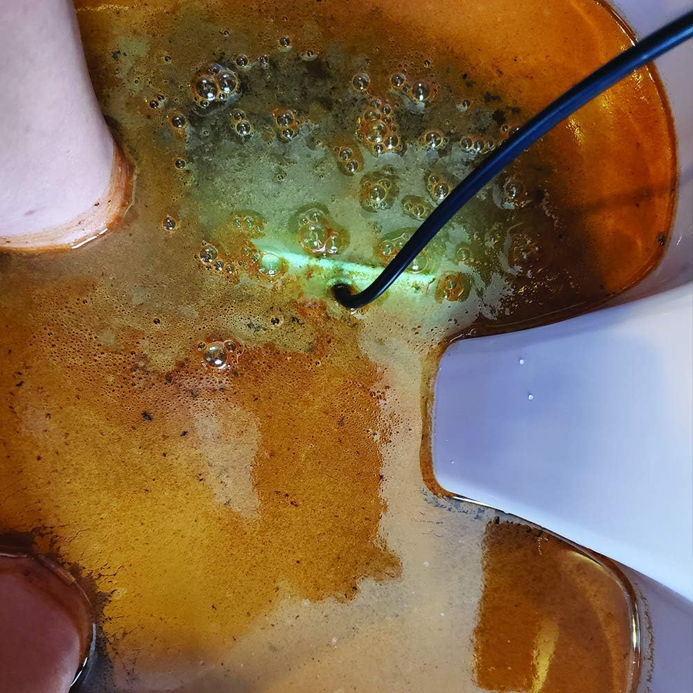 Close-up of feet in a foot bath with discolored, brownish-orange water and visible particles, indicating the results of a session.