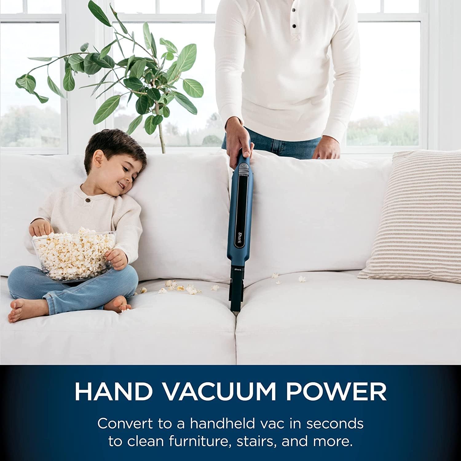 Handheld vacuum cleaning popcorn from a sofa with a child nearby