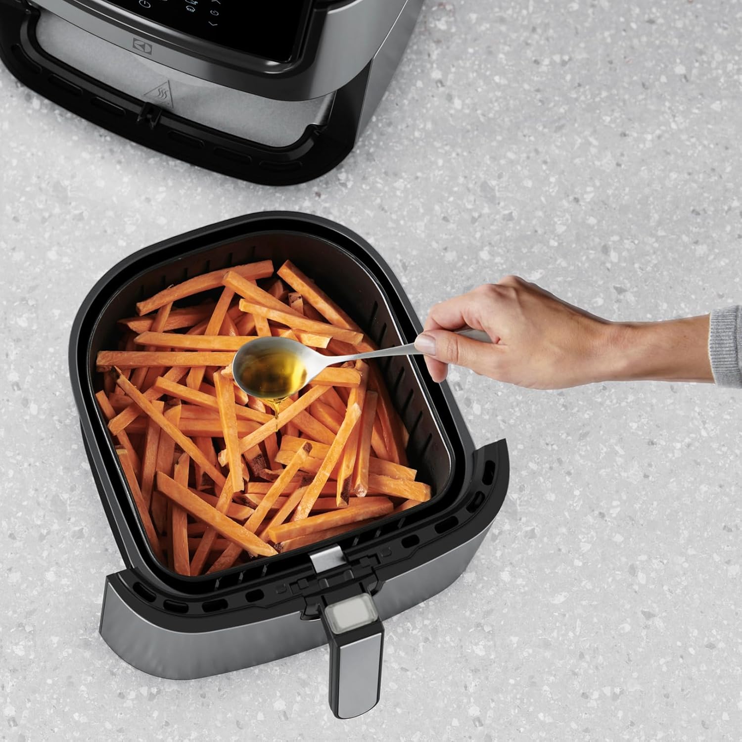 Adding oil to sweet potato fries in air fryer basket