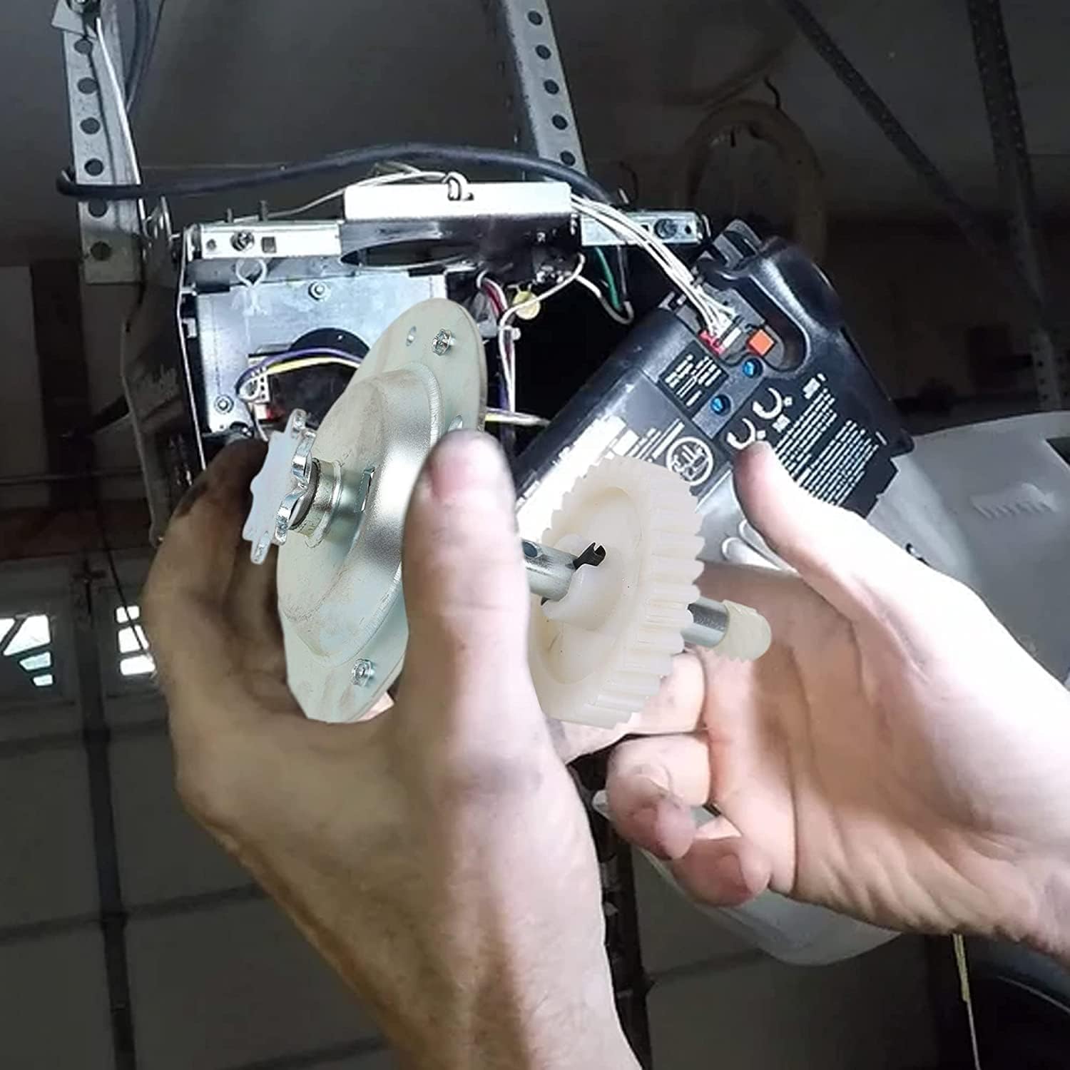 A pair of hands installing the new gear and sprocket assembly into a garage door opener mechanism, showing the alignment of the gear with the motor shaft.