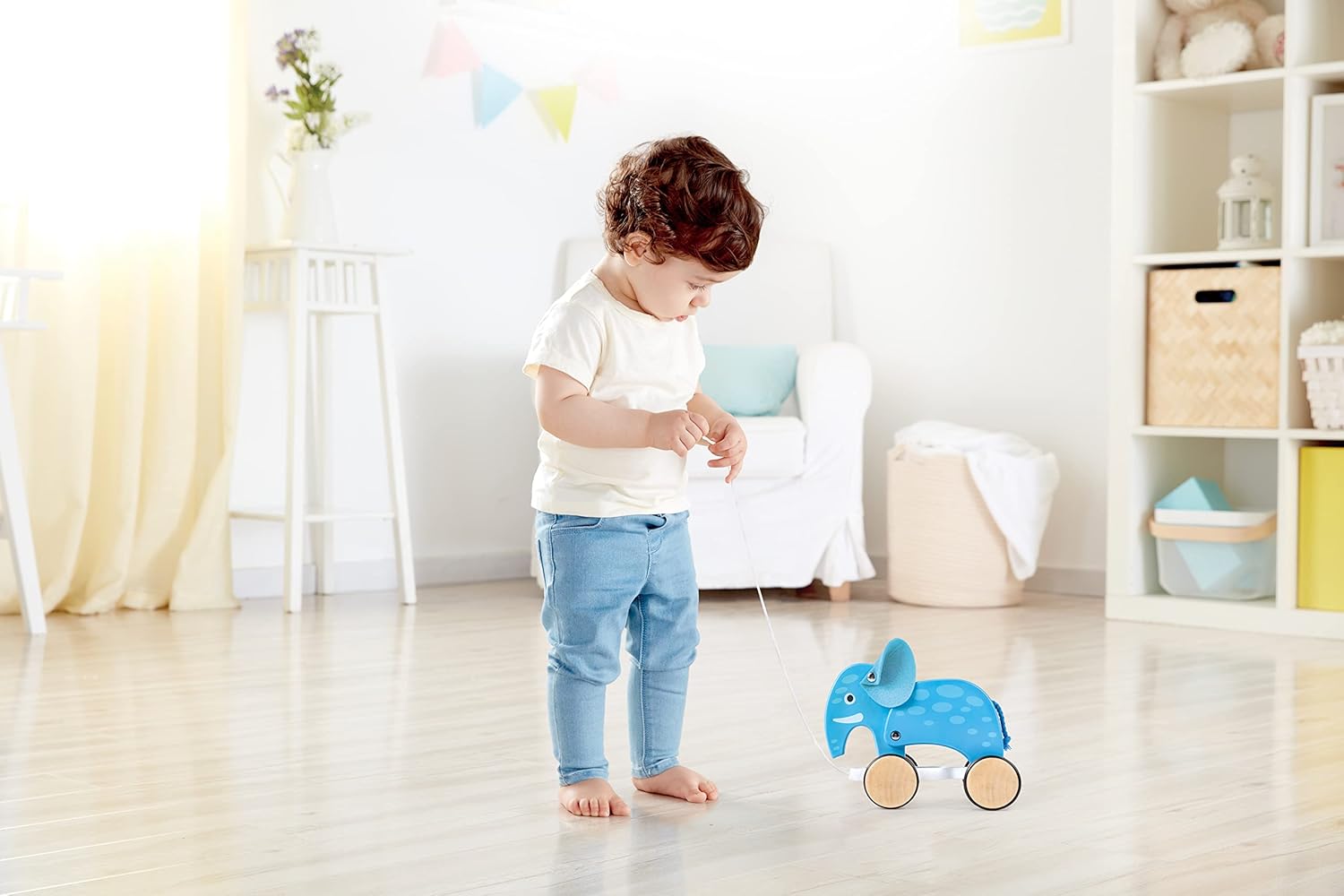 A toddler standing and pulling the Hape Elephant toy with its string.