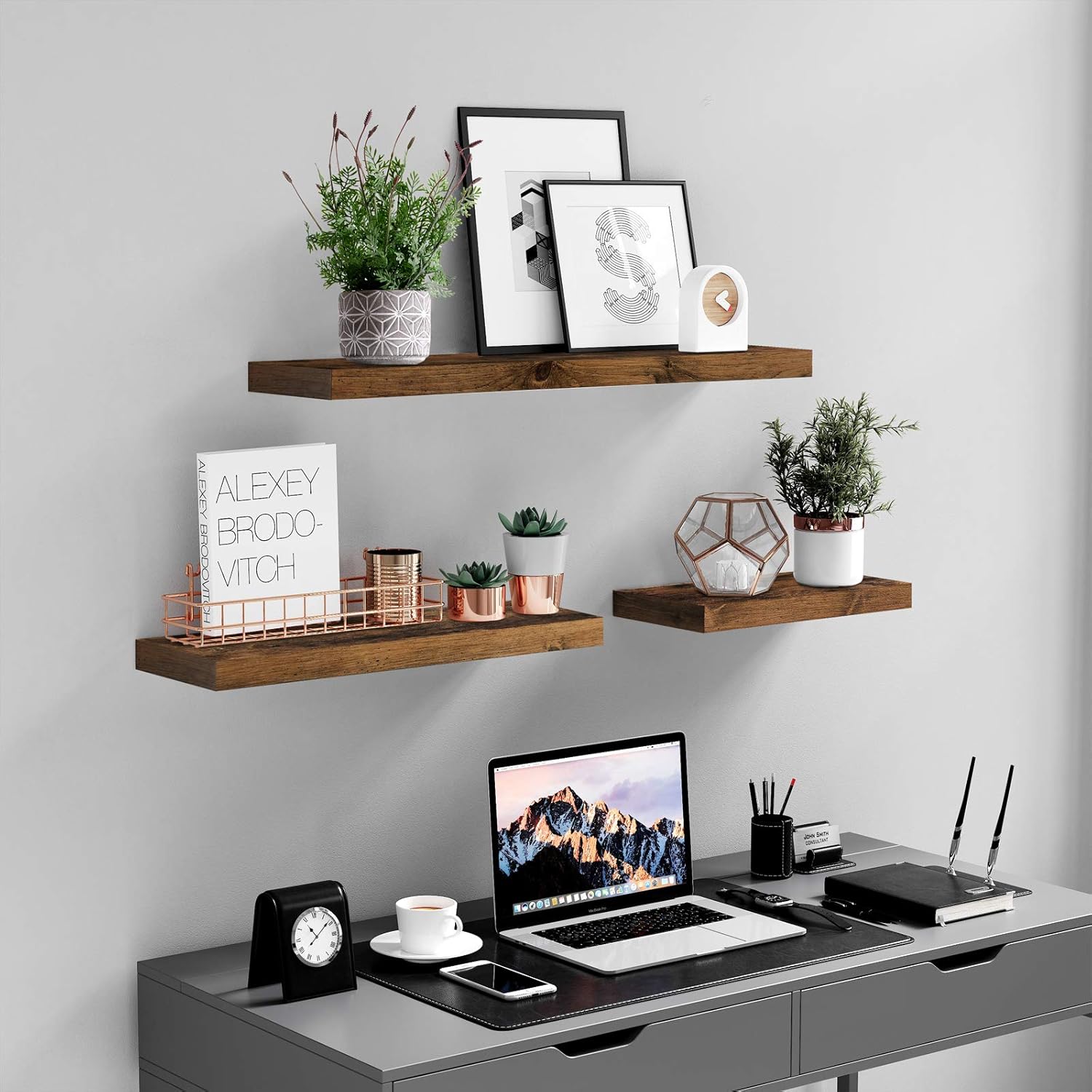 Three VASAGLE floating shelves mounted above a desk, displaying framed pictures, small potted plants, and decorative items.