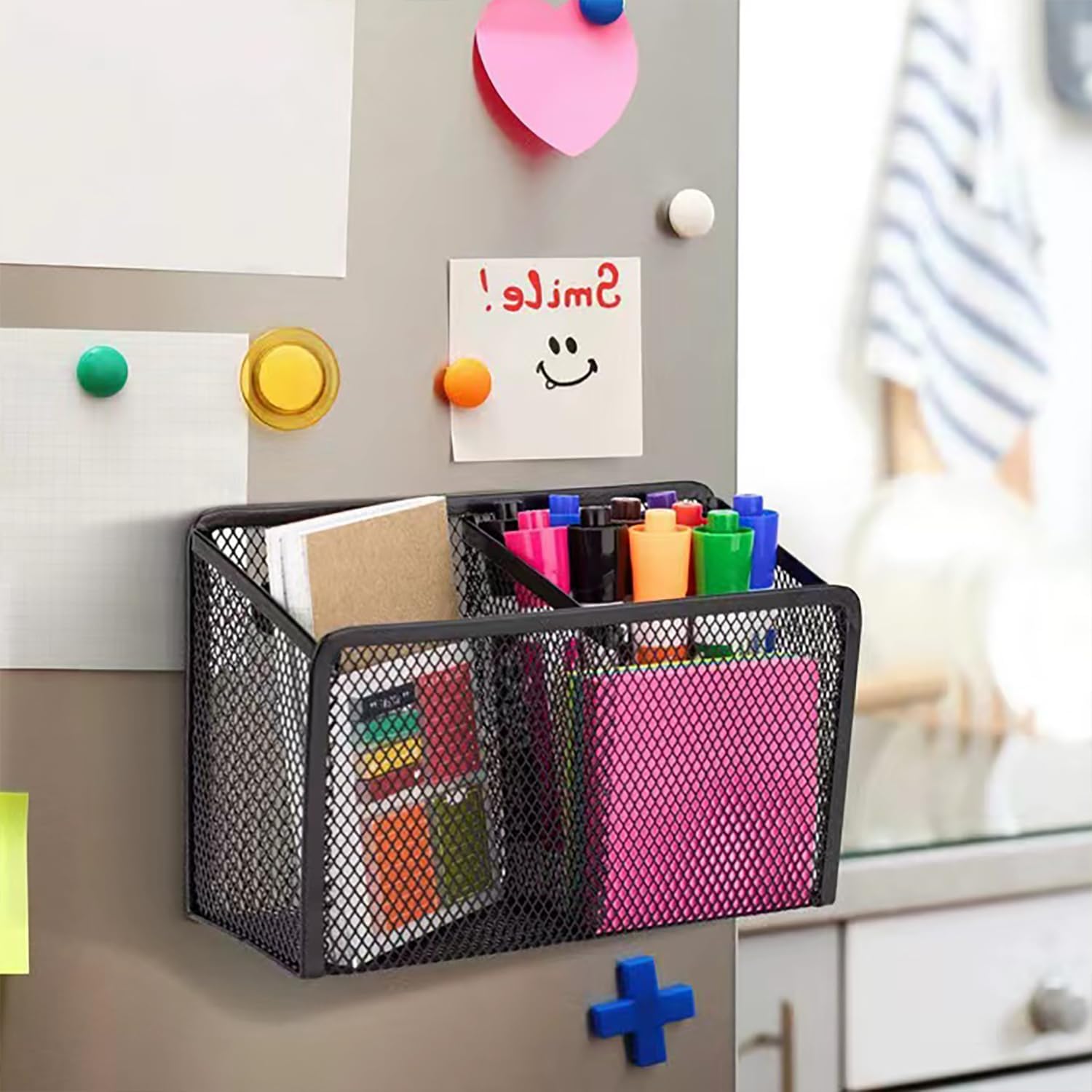 Magnetic pen holder on a refrigerator, filled with pens, markers, and small notebooks.