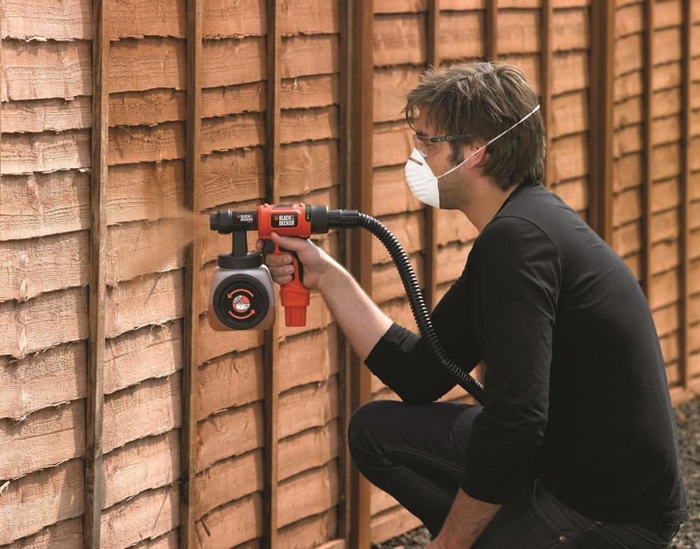 Man kneeling and spraying a wooden fence with the paint sprayer